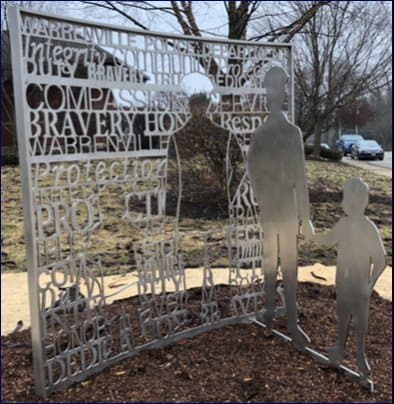 Metal Screen with words such as Duty, Bravery, Compassion, Protection, Honor, Respect, Honesty, Service, Dedication are laser cut into the metal. The top of the screen Reads Warrenville Police Department. A cut out of a policeman holding a child's hand is in the screen, while the positive cut out is welded at a 90 degree angle to the screen. Installed in Warrenville, Illinois.