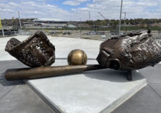 These two oversized base balls gloves and oversized baseball with the Omaha Maverick's logo and giant baseball bat sit at the entrance the entrance to the Tal Anderson Field and the Connie Claussen Field at Maverick Park. The field will provide seating for 1,500 fans, as well as additional berm seating on each baseline for fans.