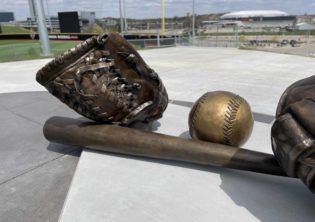These two oversized base balls gloves and oversized baseball with the Omaha Maverick's logo and giant baseball bat sit at the entrance the entrance to the Tal Anderson Field and the Connie Claussen Field at Maverick Park. The field will provide seating for 1,500 fans, as well as additional berm seating on each baseline for fans.