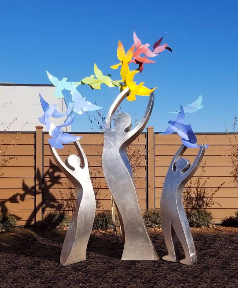 These three stainless steel figures represent a mother, and her two children, a boy and a girl. Their arms joyously reach upward as a rainbow of birds fly from their arms. Representing the endless possibilities that tomorrow brings. Located in