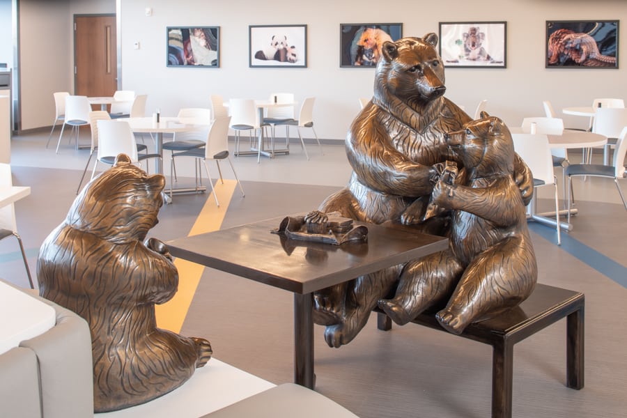 Mother bear with her two cubs, sitting at a table in the cafeteria eating lunch. One cub is eating out of a jar of honey, while the other is eating a paenut butter and jelly sandwich. The mama bear is claening the sandwich eating bear's face with a napkin. Bronze sculpture in Children's Hospital and Medical Center in Omaha, Nebraska.